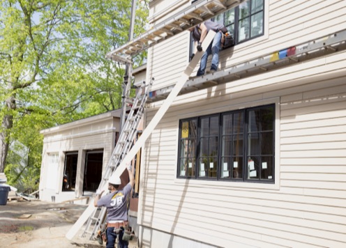 在房屋建筑工地，一名工人正在把墙板递给另一名工人。